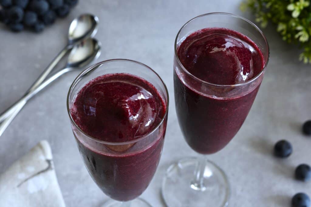 Two flute glasses of Concord grape sorbet with spoons on a table.