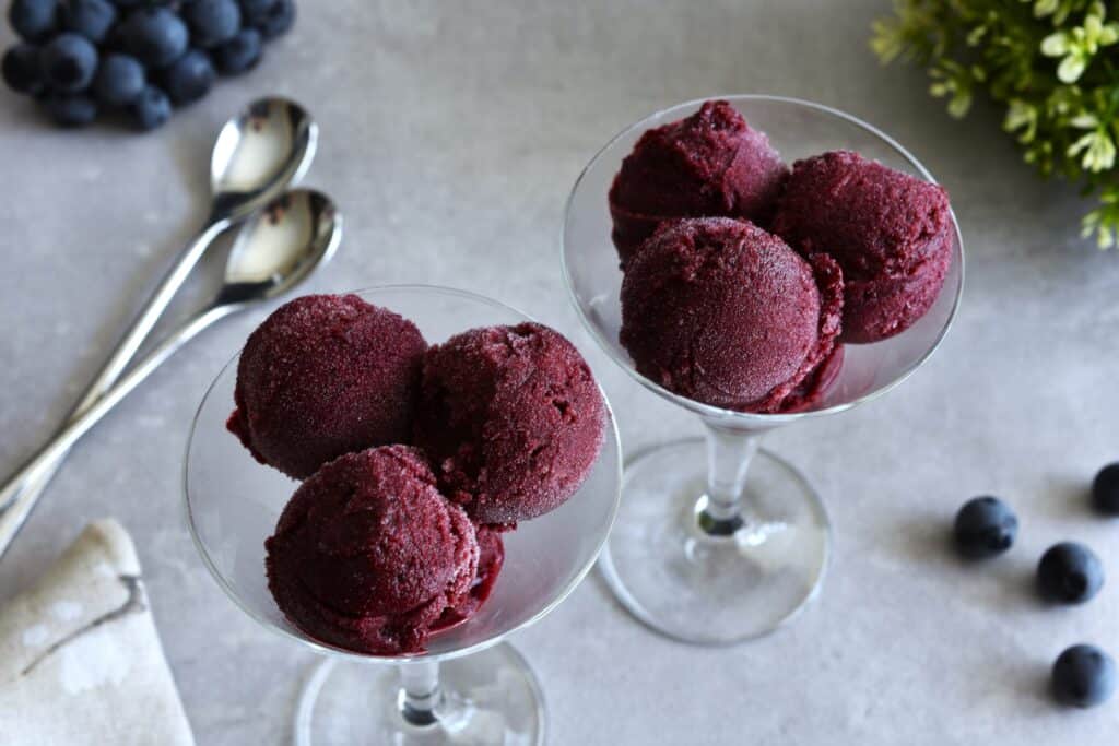 Two glasses with scoops of Concord grape sorbet on a table.