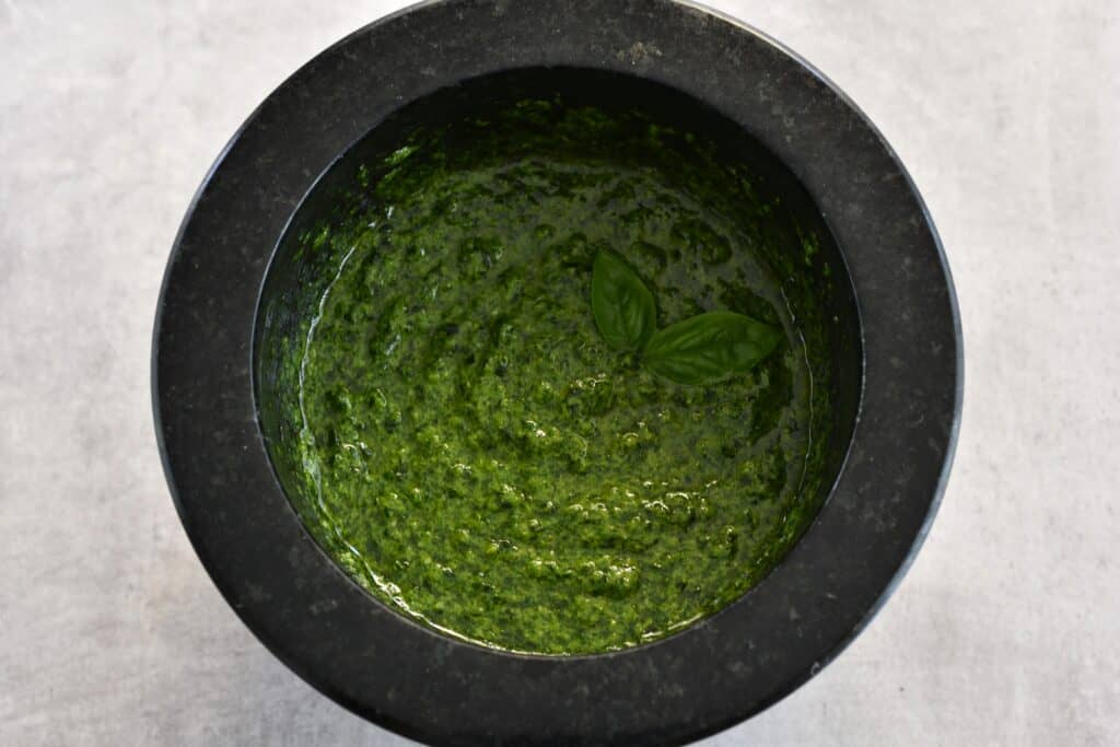 Vegan basil pesto in a mortar with a garnish of basil leaves.