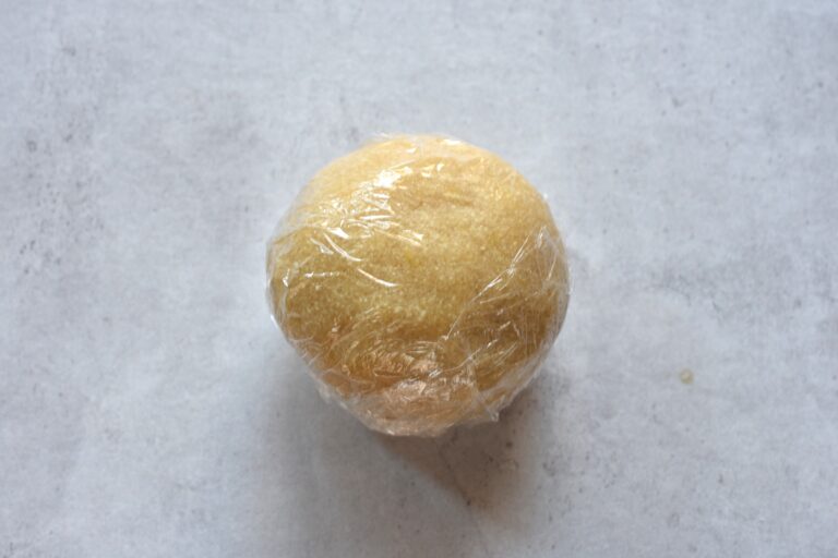 A ball of vegan Italian almond biscuit paste wrapped in clingfilm.