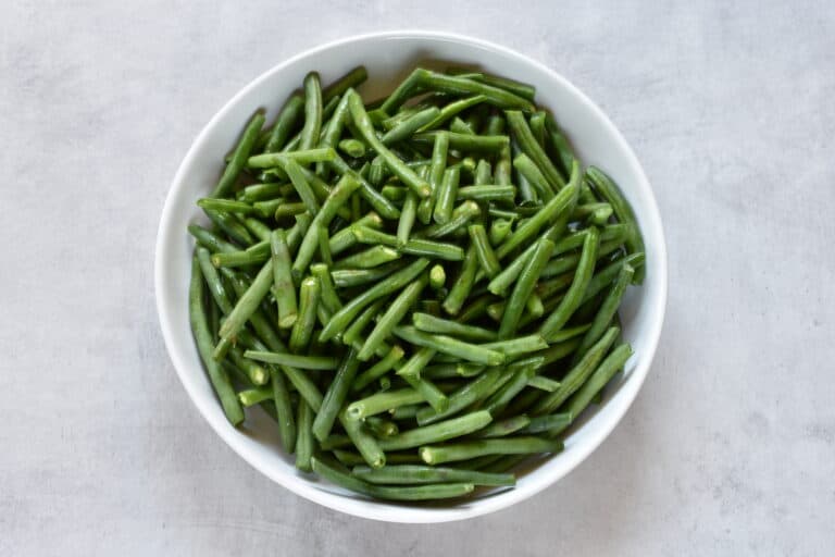 A bowl of raw green beans, washed and trimmed, in a white bowl.