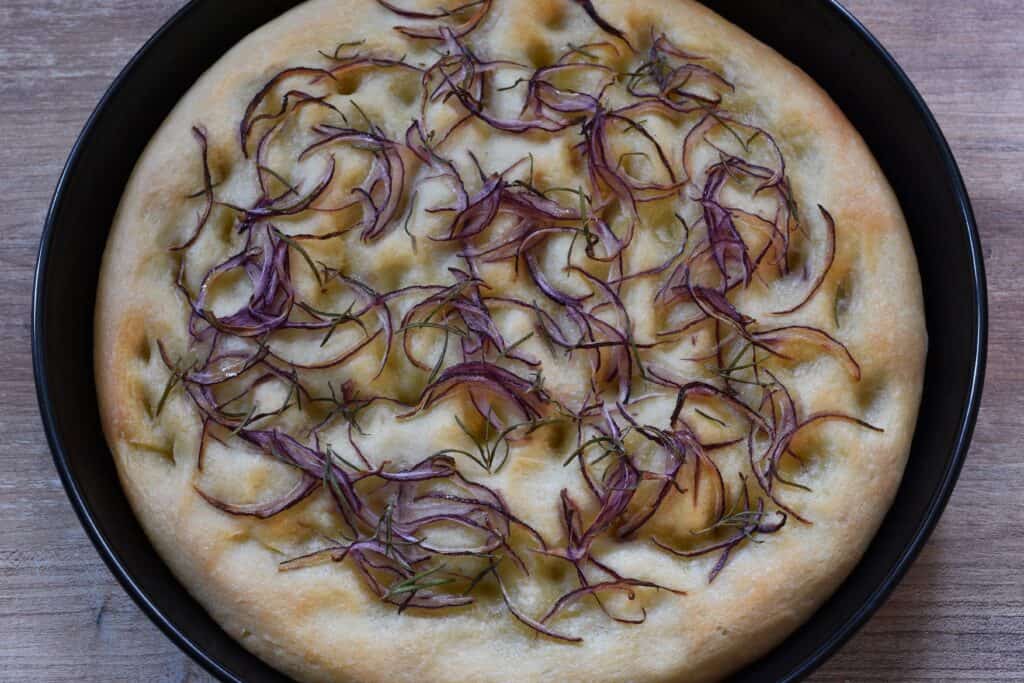 A close-up image of red onion and rosemary focaccia in a tin.