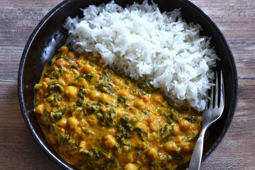 A plate of quick vegan chickpea and spinach curry with fluffy white basmati rice and a fork.