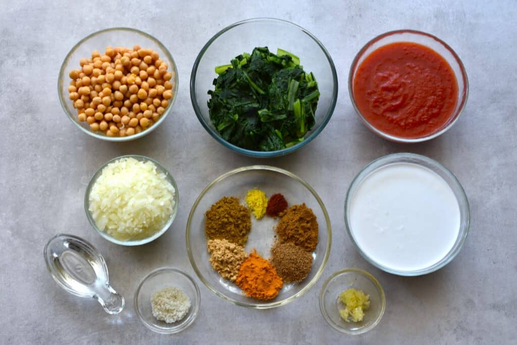 Ingredients for quick vegan chickpea and spinach curry in individual glass bowls on a worktop.