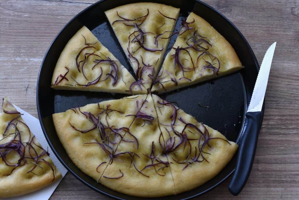 Six slices of focaccia dough in a tin with a knife.