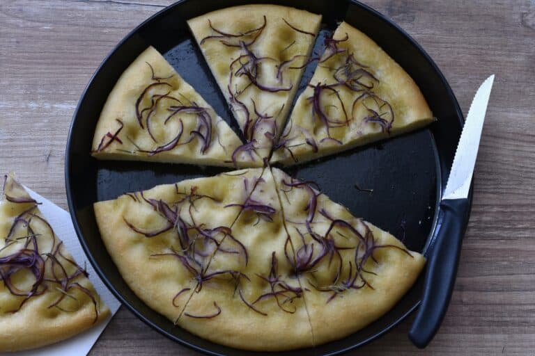 Six slices of red onion and rosemary focaccia in a round baking tin with a knife.