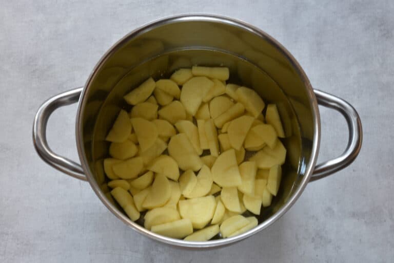 Sliced potatoes in a pan of cold water.