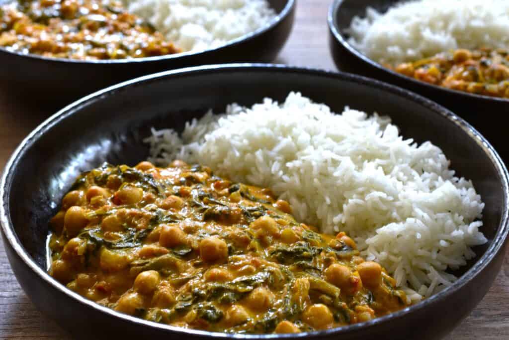 Three plates of quick vegan chickpea and spinach curry with white basmati rice.