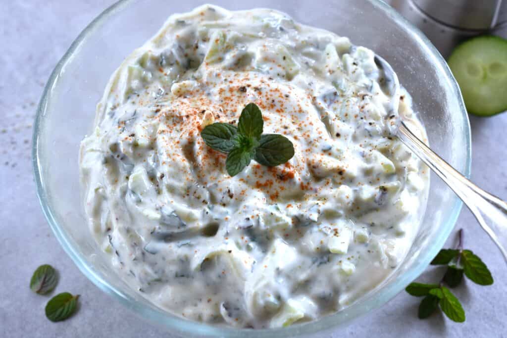 Vegan cucumber raita in a glass bowl with a spoon.