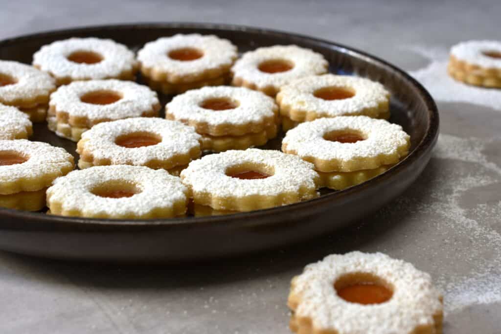 Vegan spitzbuben biscuits with apricot jam filling on a brown plate on a kitchen worktop.