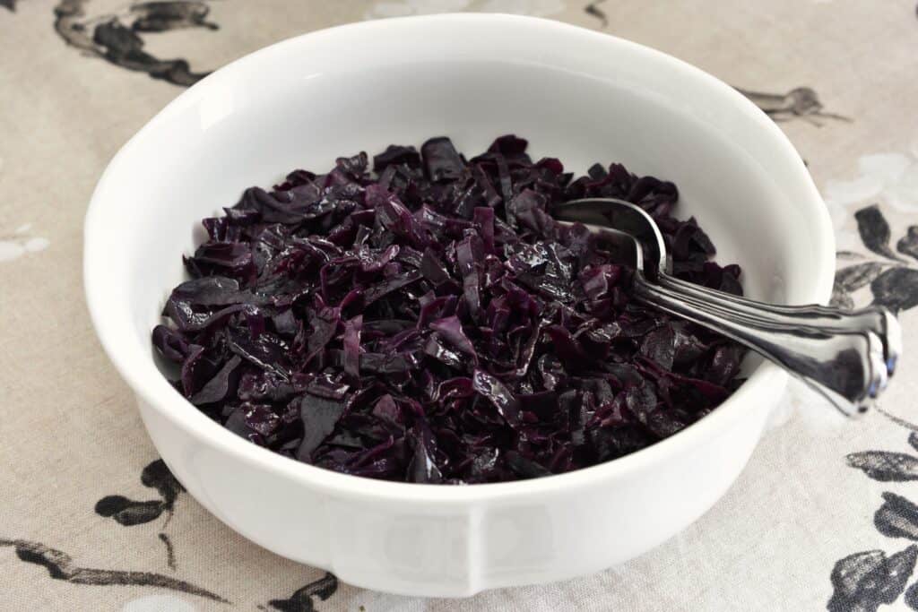 Vegan braised red cabbage Italian style with balsamic vinegar in a white serving bowl with a fork and spoon.