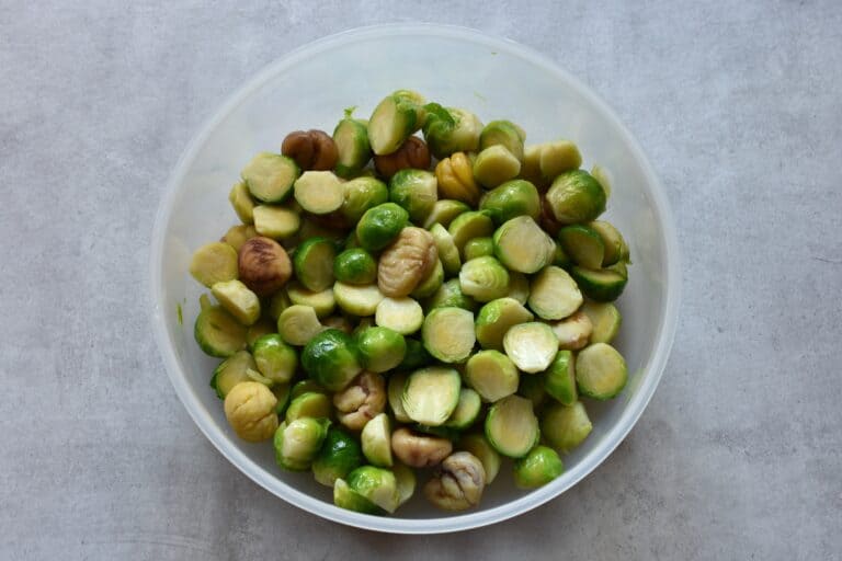 Brussels sprouts and chestnuts tossed in oil in a plastic bowl.