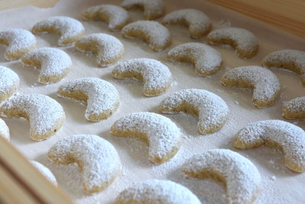 Vegan Vanillekipferl (vanilla crescent cookies) on a sheet of baking paper in a wooden box.