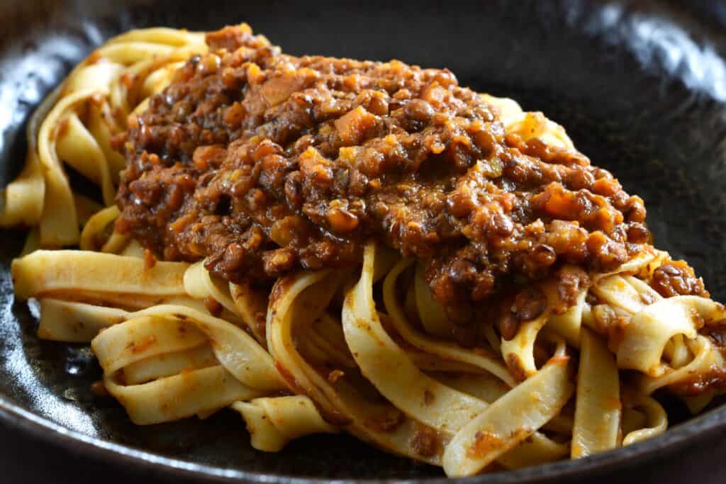 A close-up image of tagliatelle with vegan ragu on a dark plate.