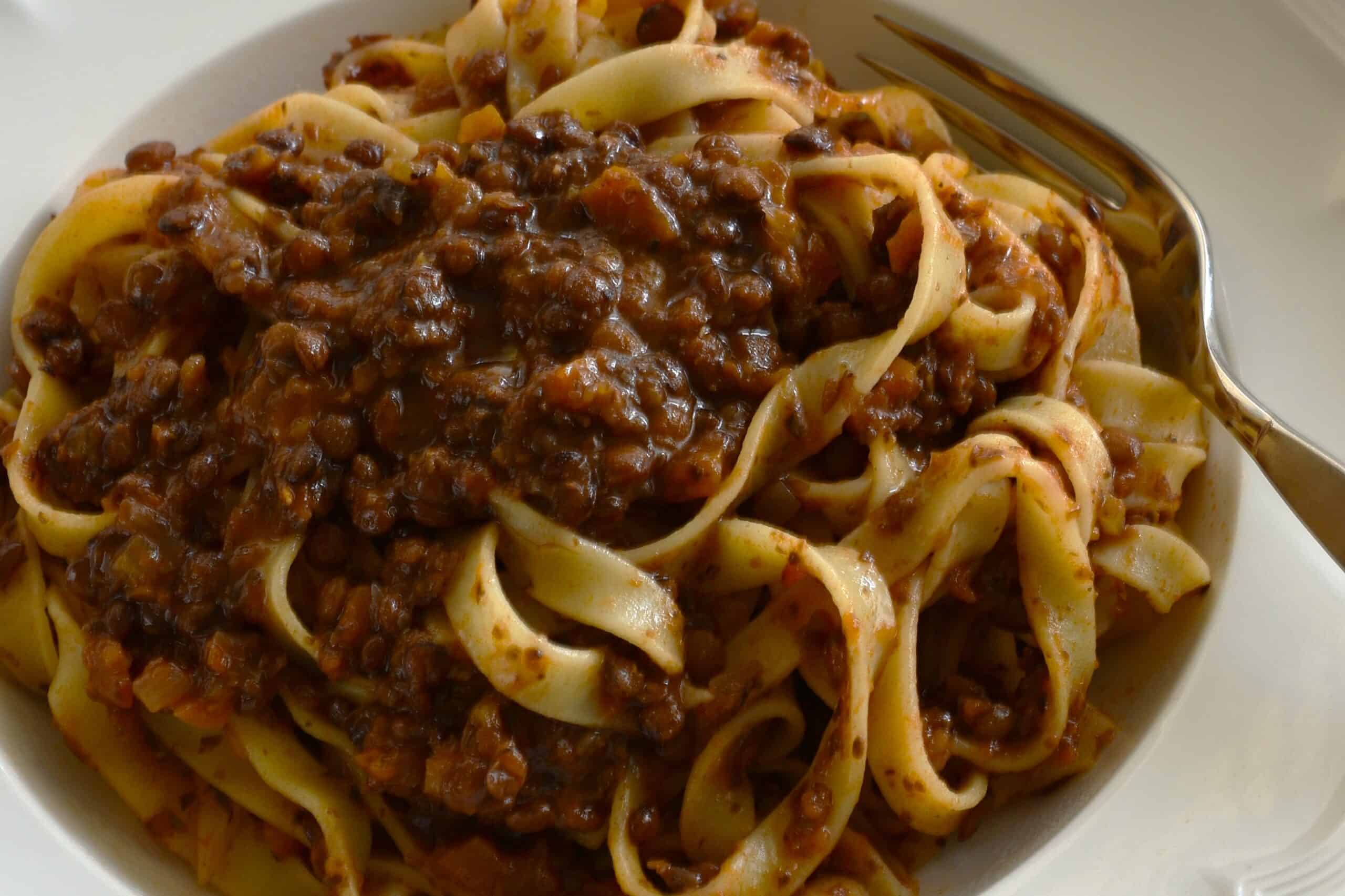 A close-up image of tagliatelle with vegan ragu on a white plate with a fork.