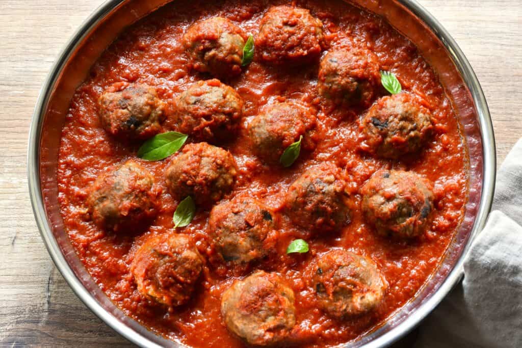 Polpette di melanzane vegan eggplant meatballs in tomato sauce with a garnish of basil leaves in a pan.