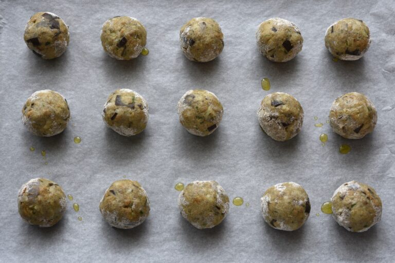 Polpette di melanzane vegan eggplant meatballs brushed with oil on a baking tray.