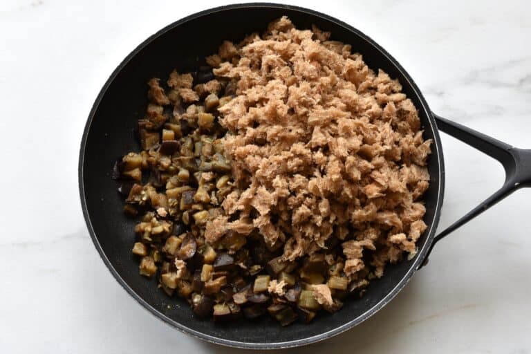 Sautéed aubergine/eggplant and pieces of bread in a pan.