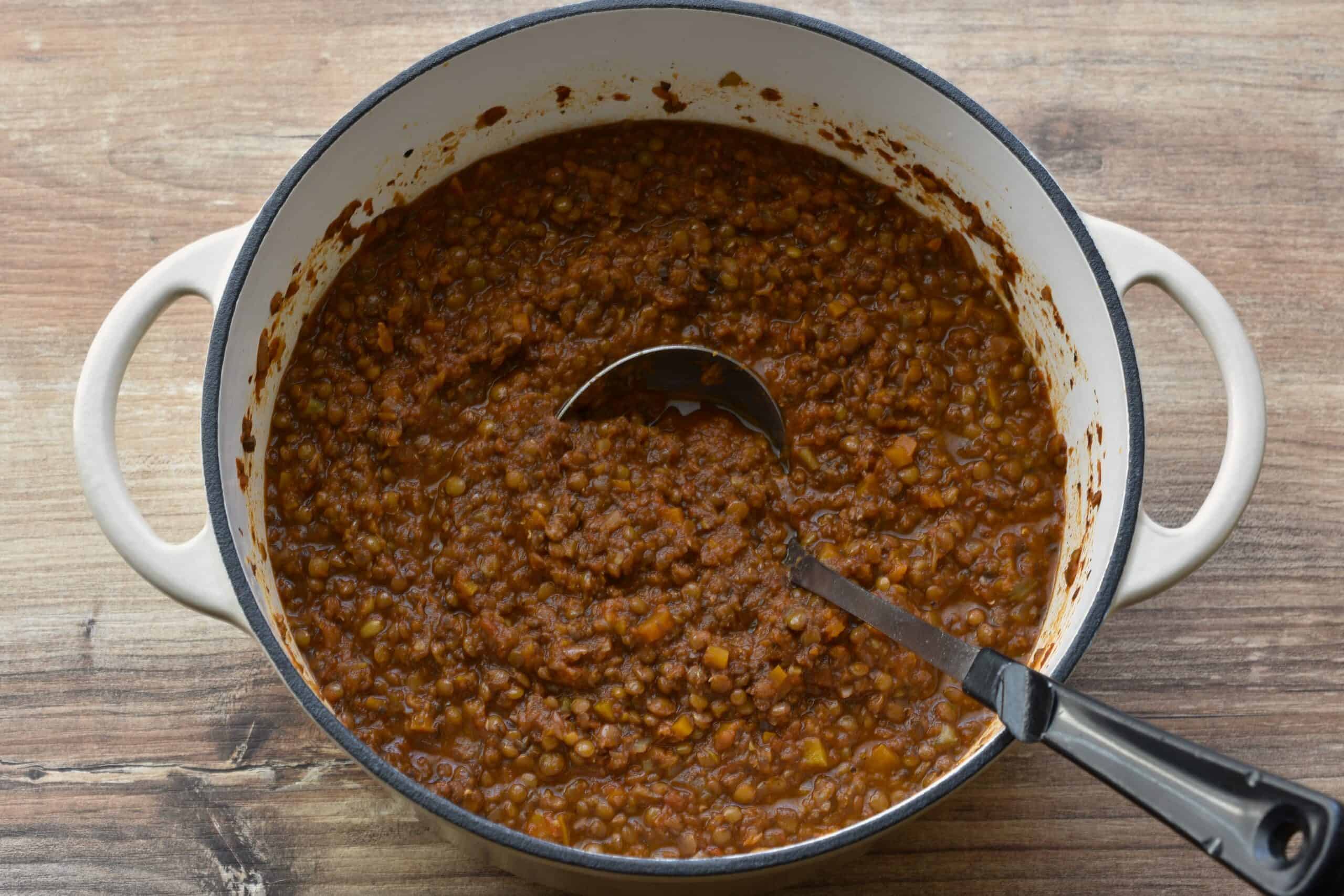 Vegan lentil ragu in a white cast iron pan with a ladle.