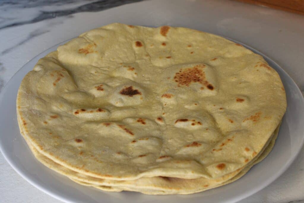 Four piadinas (Italian flatbread) made with all-purpose white flour, stacked up on a plate on a kitchen worktop.