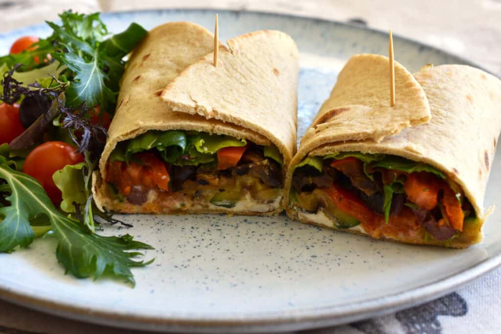 A vegan piadina rolled up, with a filling of vegan cashew cream cheese with horseradish, grilled vegetables, cherry tomatoes, mixed leaf salad, and black olives.