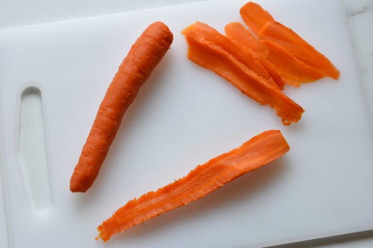 A whole slow-baked carrot and slices of carrot on a chopping board.