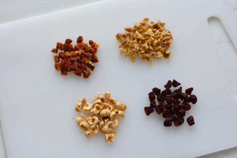 Chopped walnuts cranberries, hazelnuts, and cape gooseberries on a chopping board.