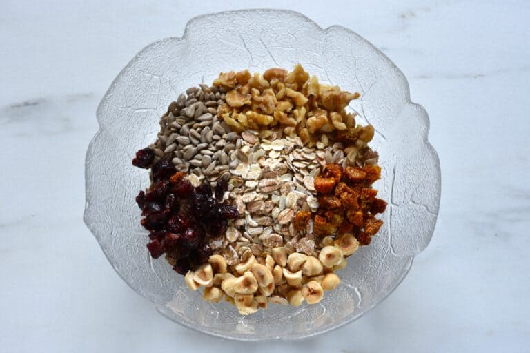 Dried cranberries and goldenberries, sunflower seeds and chopped hazelnuts and walnuts in a glass bowl.