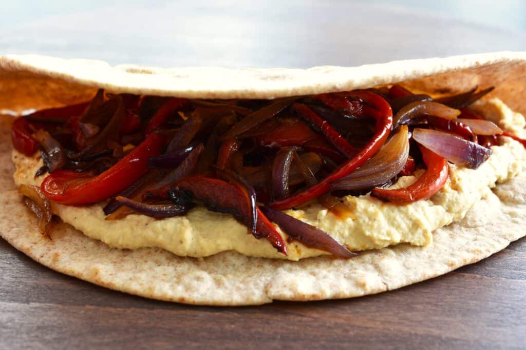 A vegan piadina (Italian flatbread) with a filling of caramelised red peppers and red onion, chickpea hummus, and black olives.