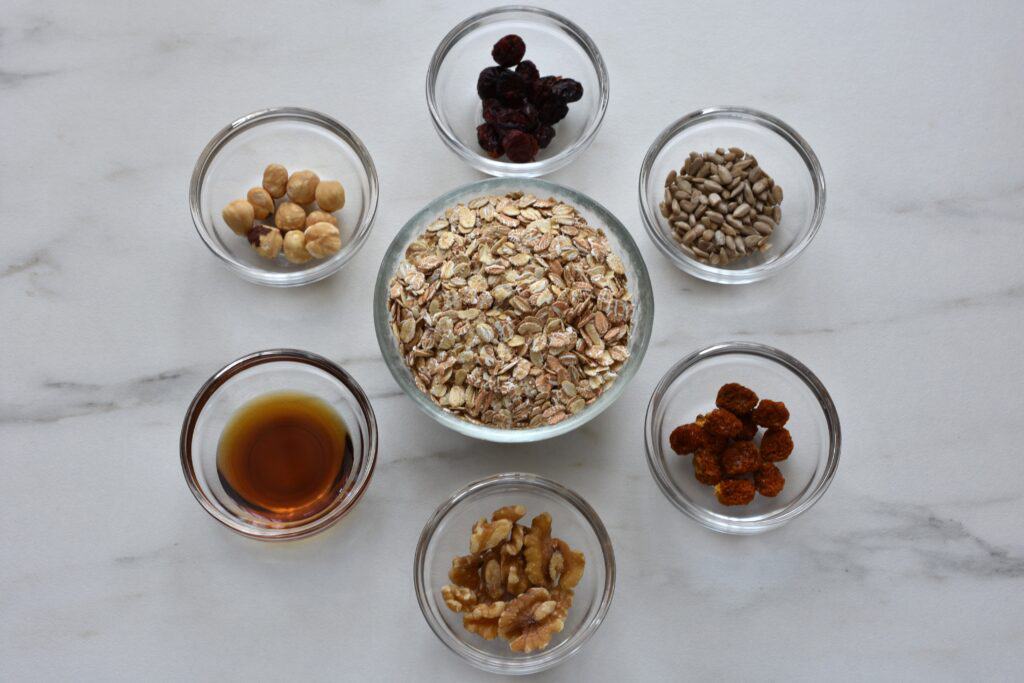 Dried cranberries, sunflower seeds, dried cape gooseberries, walnuts, maple syrup and hazelnuts in individual glass bowls.