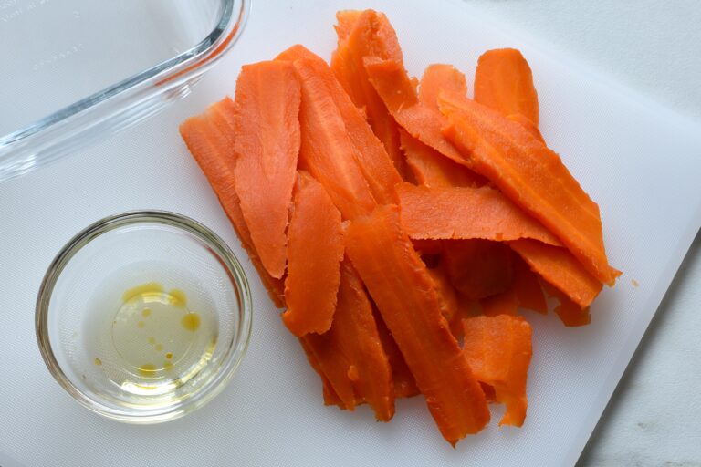 Slices of carrot and a bowl of marinade on a chopping board.