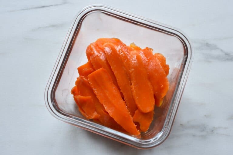 Slices of carrot in marinade in a glass container.