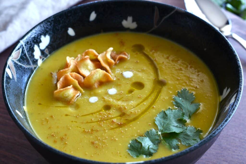 Spicy parsnip soup in a black bowl with a garnish of parsnip chips, and green coriander leaf.