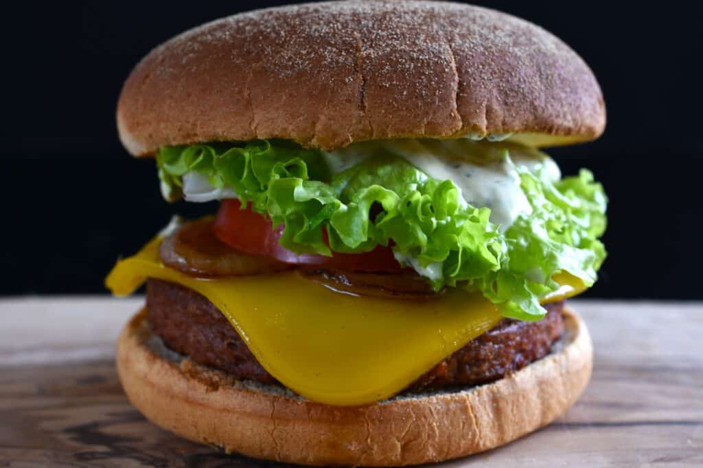 A close-up image of a vegan cheeseburger on a wooden board.