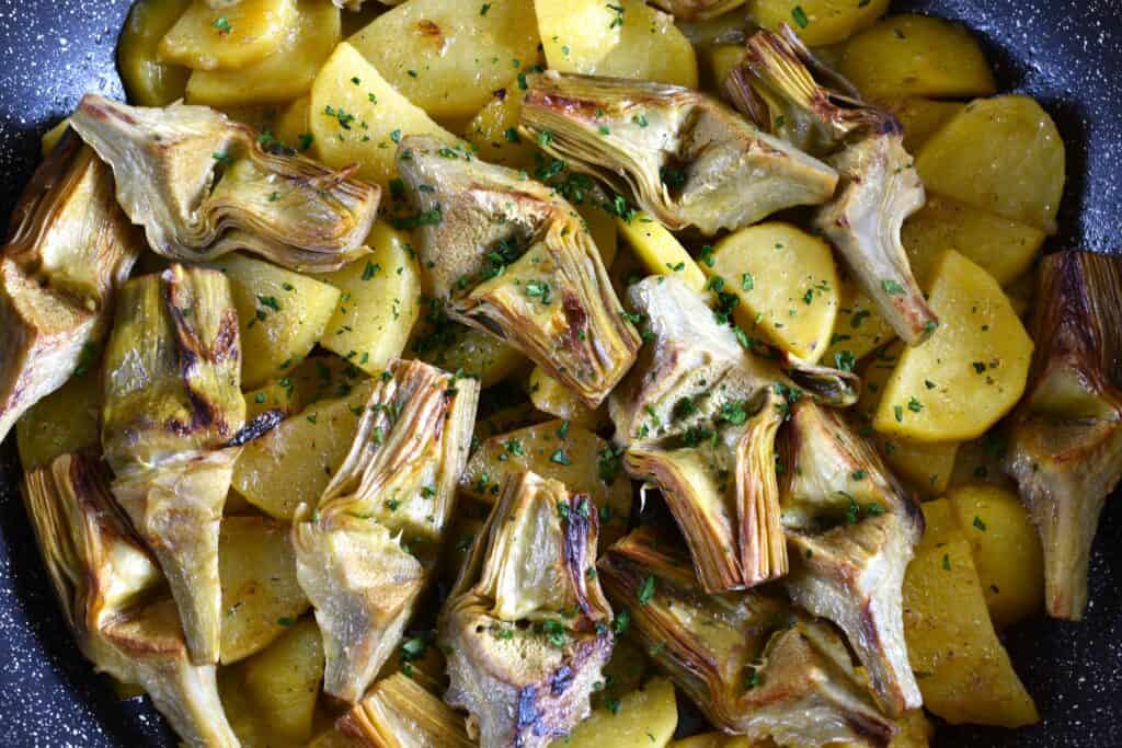 A close-up image of artichokes and potatoes in a pan.