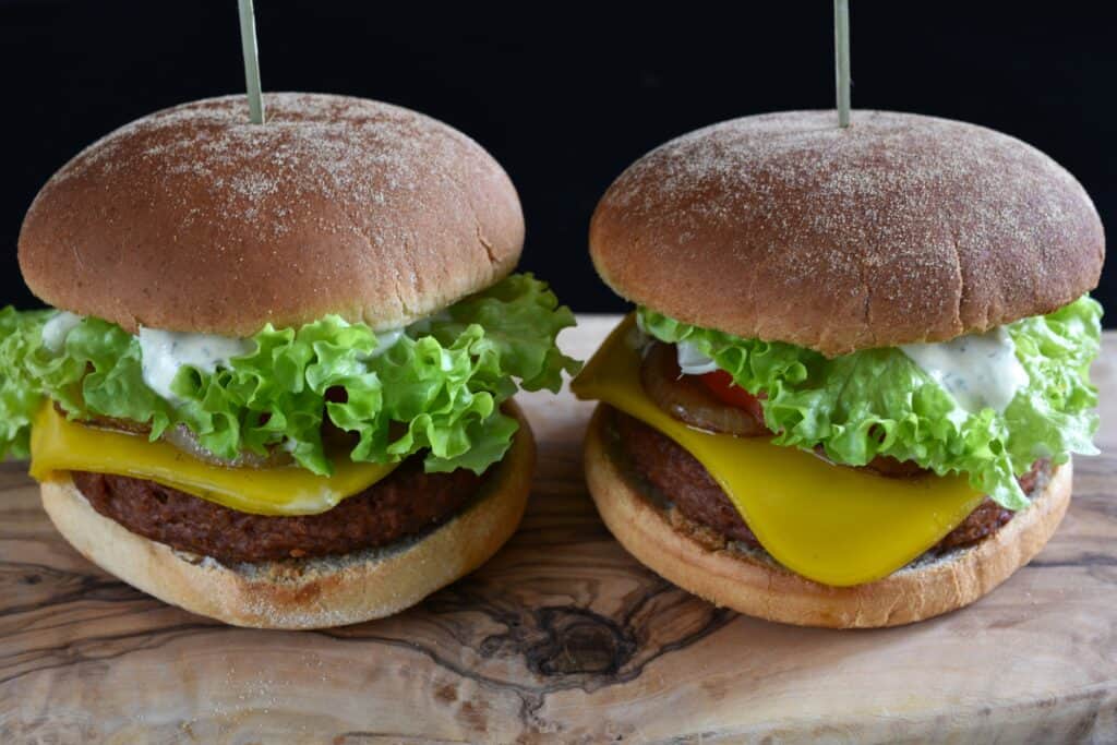 A close-up image fo two vegan cheeseburgers on a wooden board.