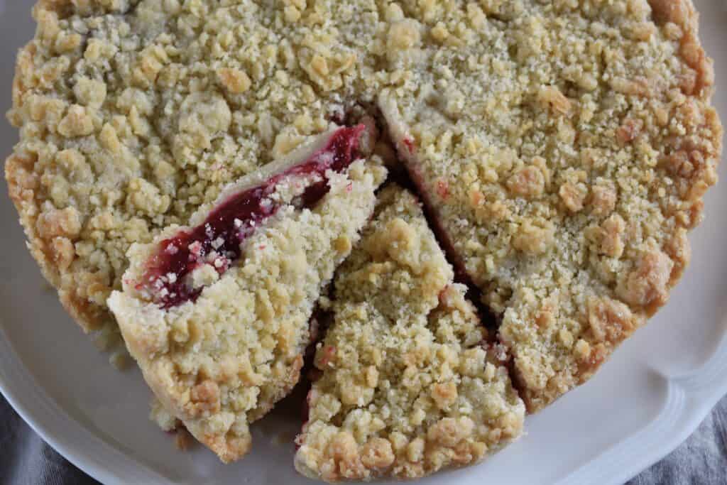 A close-up image of vegan Italian crumble cake (sbriciolata or sbrisolona) with raspberry jam filling.