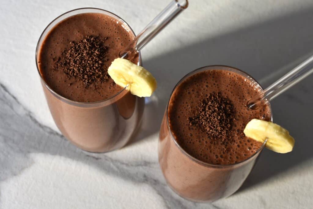 A close-up of two glasses of vegan chocolate banana protein shake.