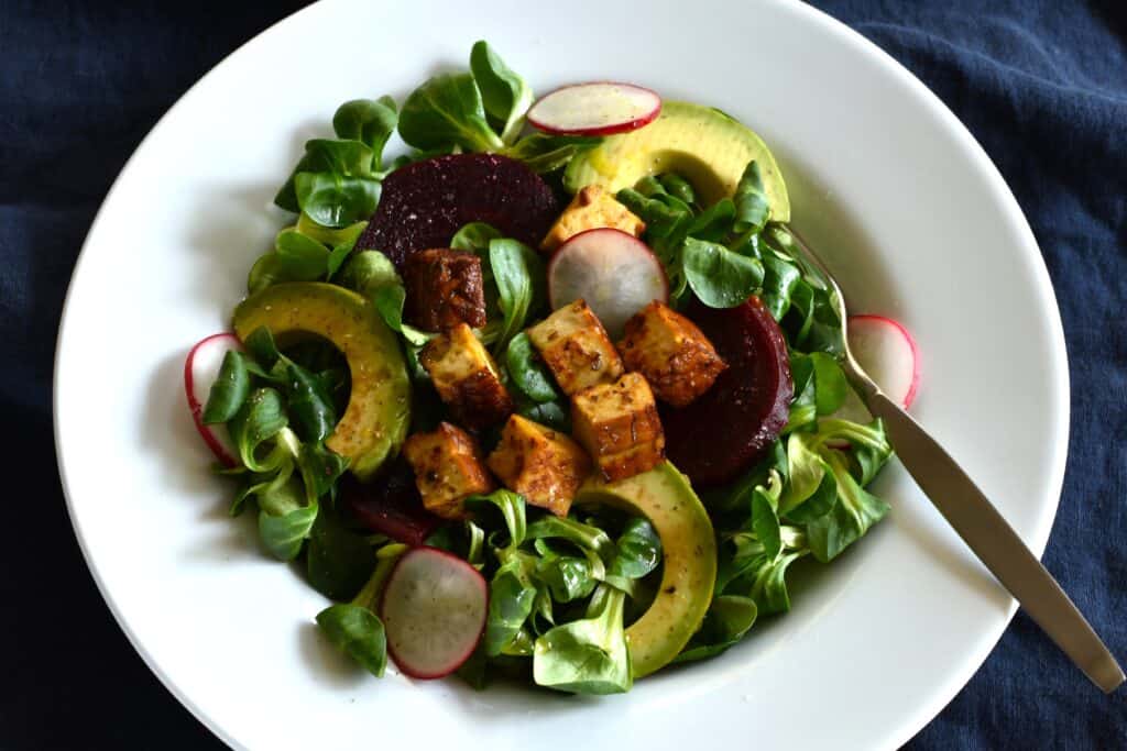 A plate of lamb's lettuce salad with smoked tofu, beetroot, avocado and radishes.