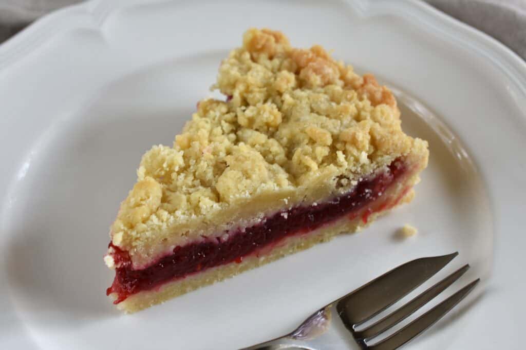 A slice of Italian crumble cake (sbriciolata or sbrisolona) with raspberry jam filling on a plate with a fork.