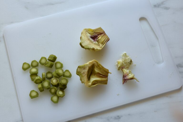 A trimmed artichoke cut in half on a chopping board.