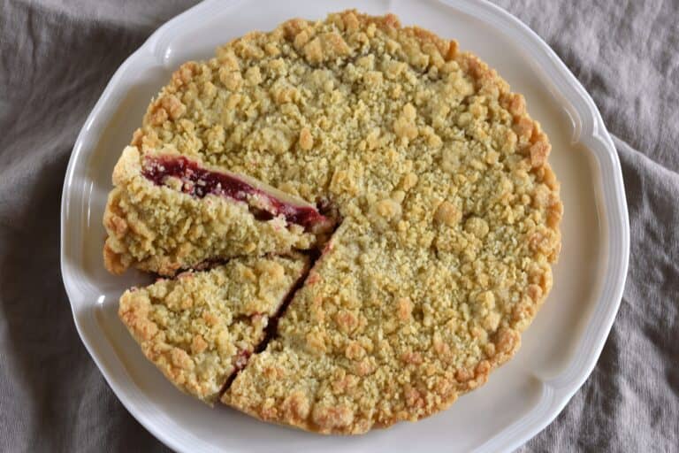 A vegan crumble cake (sbriciolata) with a raspberry jam filling on a white plate.