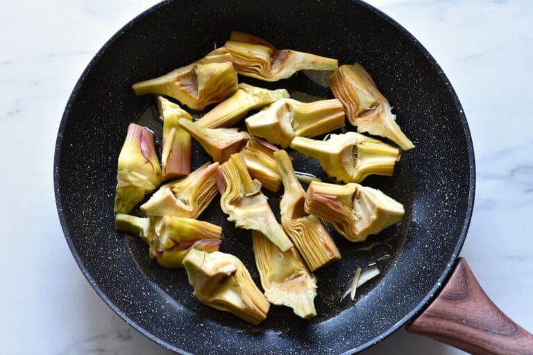 Artichoke quarters in a pan with olive oil.