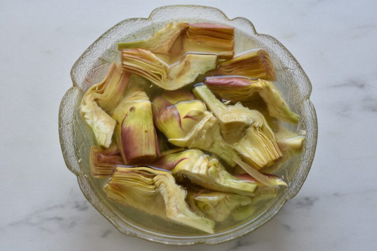 Artichoke quarters in a bowl of water and lemon juice.