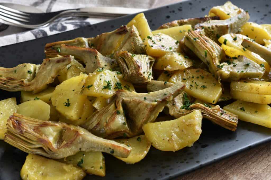 Braised artichokes and potatoes on a black serving plate with a spoon and fork.