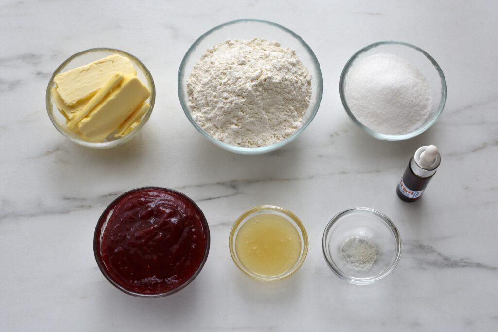 Flour, sugar,  salt, vegan butter, vanilla extract, aquafaba, and raspberry jam in individual glass bowls.