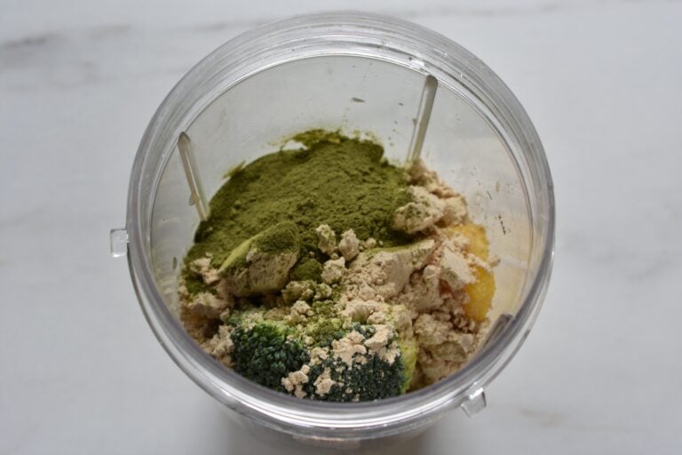 Pineapple, coconut, banana, broccoli, moringa, protein powder, and pineapple juice in a blender beaker.