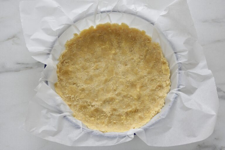 Raw vegan crumble mixture pressed down to form the base of the cake in a dish lined with greaseproof paper.