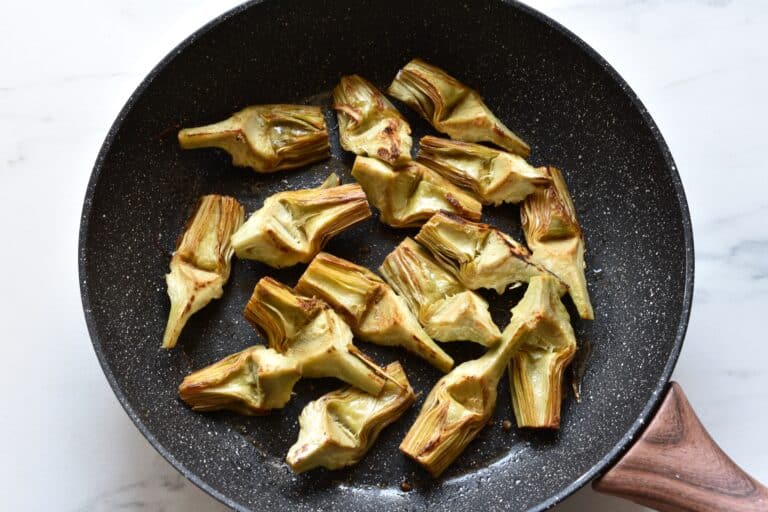 Sautéed artichoke quarters in a pan.