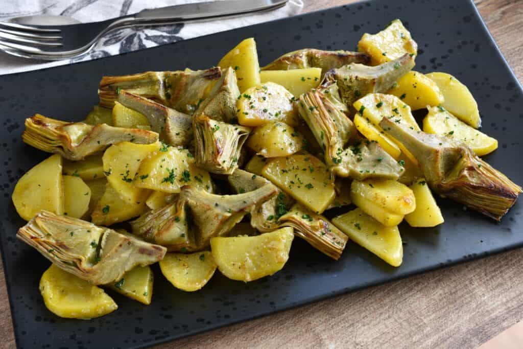 Sautéed artichokes and potatoes on a black serving dish.